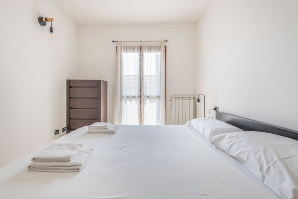 A bedroom with a bed, a dresser, a radiator, and a window with curtains.