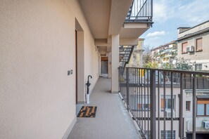 A narrow corridor with a doormat, a door, and a railing leading to a balcony.