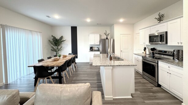 A modern kitchen with white cabinets, a granite countertop, stainless steel appliances, and a dining area with a wooden table and chairs. - Modern 3br/2.5ba • 3 king bed • Gameroom • Pets OK (Montgomery)