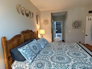 A bedroom with a wooden headboard, patterned bedding, a bedside lamp, and a view into the bathroom. - Sabino Sanctuary Townhome (Tucson)