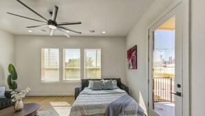 Ein Schlafzimmer mit Bett, Deckenventilator, Fenstern und einer Tür, die auf einen Balkon führt.