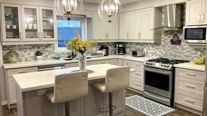 Uma cozinha moderna com uma ilha central, banquetas, fogão, micro-ondas e vista para o exterior.