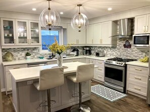 A modern kitchen with a central island, bar stools, a stove, microwave, and a view of the outdoors. - Perfect Falls Location retreat (Niagara Falls)