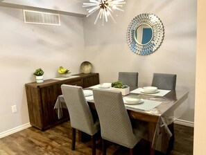 A dining area with a wooden table, grey upholstered chairs, a decorative mirror, and a ceiling light fixture. - Perfect Falls Location retreat (Niagara Falls)