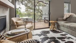 Una sala moderna con sofá, sillón y una mesa de centro. Hay una puerta de cristal que da a un patio exterior.