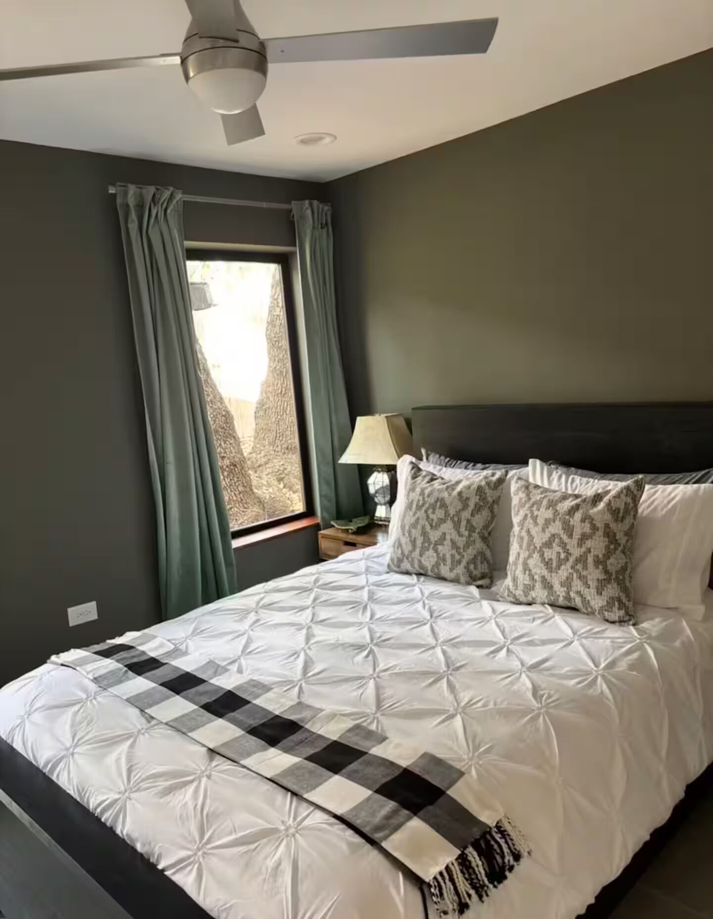A bedroom with a bed, a ceiling fan, a window with curtains, and a bedside lamp.