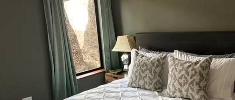 A bedroom with a bed, a ceiling fan, a window with curtains, and a bedside lamp.