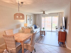 A living room with a dining table, wicker chairs, a sofa, a TV, and a ceiling fan. - The Scenic Retreat at Ciboney 4010 - Gulfview - 3-bedroom - Pet Friendly (Miramar Beach)