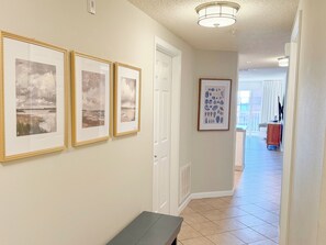 A hallway with framed artwork on the wall, a bench, and a door leading to another room. - The Scenic Retreat at Ciboney 4010 - Gulfview - 3-bedroom - Pet Friendly (Miramar Beach)