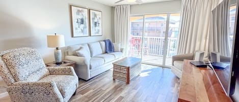 Una sala de estar con un sillón estampado, un sofá, una mesa de centro y un mueble para televisor.