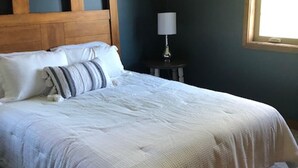 Ein Schlafzimmer mit hölzernem Kopfteil, einem Bett mit weißer Bettwäsche, einem Nachttisch mit Lampe und einem Fenster.