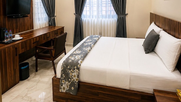 Una habitación de hotel con cama, escritorio, silla, televisión y ventilador de techo.