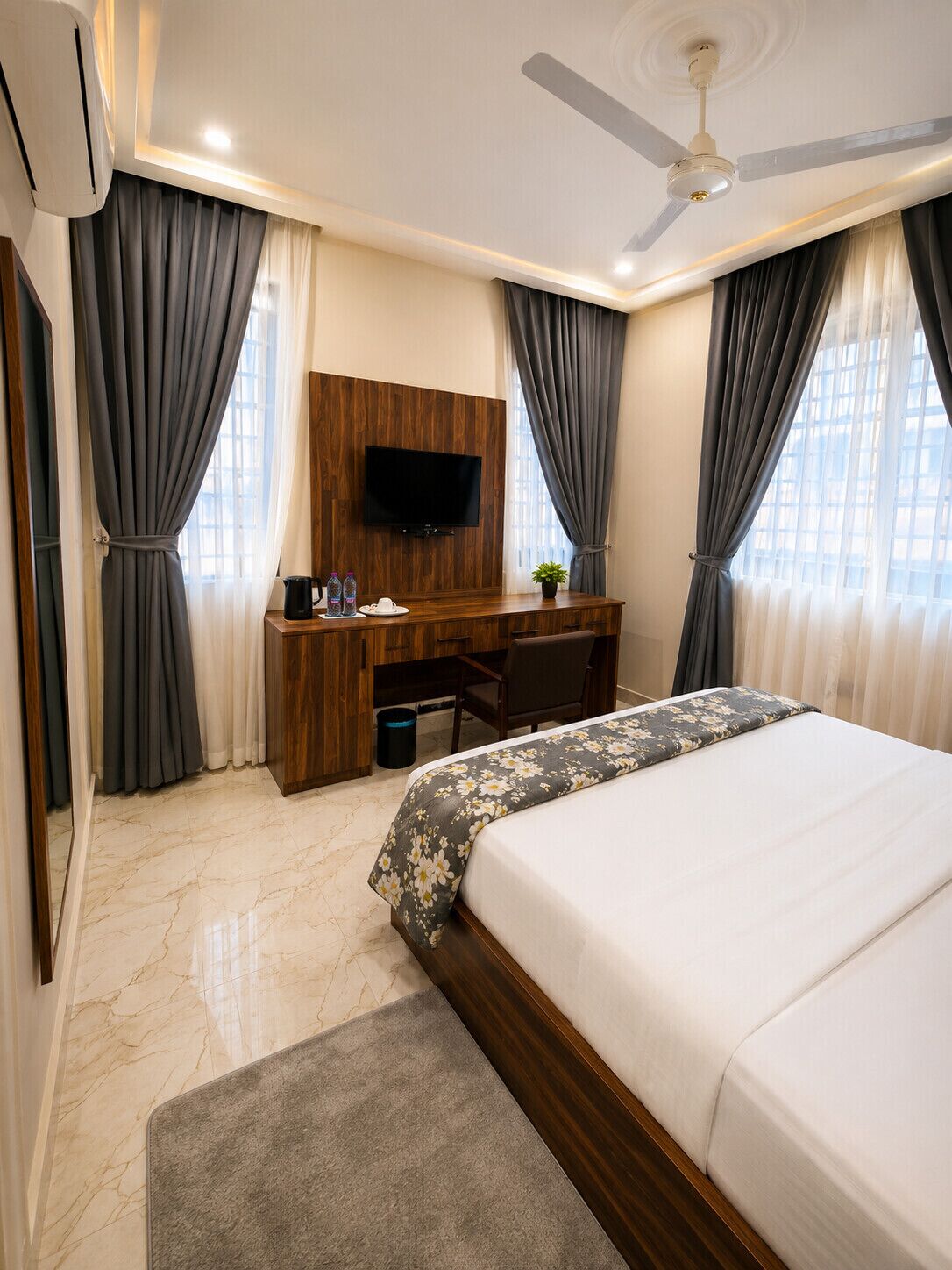 Habitación de hotel con cama, escritorio, televisor y ventilador de techo.