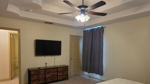 A bedroom with a bed, a dresser, a ceiling fan, a TV, and a door.