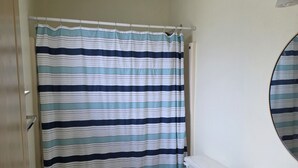 A bathroom with a striped shower curtain, a toilet, a sink with a soap dispenser, and a mirror.