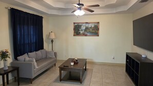 A living room with a sofa, coffee table, lamp, painting, ceiling fan, and TV stand.