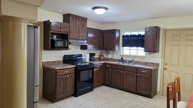 A kitchen with dark wooden cabinets, a black stove, a microwave, and a window with a curtain.