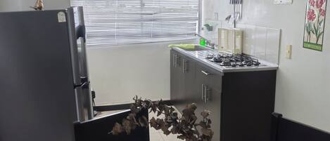 Una cocina moderna con una mesa de comedor de vidrio, un refrigerador, una estufa y una ventana con persianas.