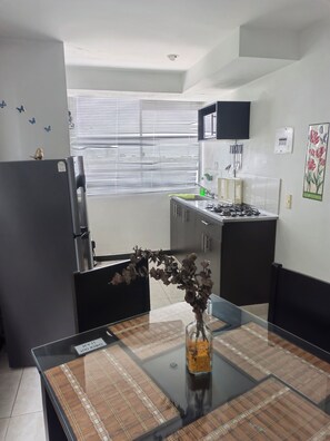 Una cocina moderna con una mesa de comedor de vidrio, un refrigerador, una estufa y una ventana con persianas.