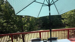 Um terraço com mesa, cadeiras, um guarda-sol e vista para o verde ao redor.