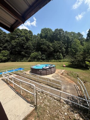 A swimming pool with a surrounding deck and a covered area, set against a backdrop of dense trees and a clear sky. - Private Lake House (Covington)