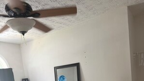 Um quarto com cama, ventilador de teto, quadro emoldurado e guarda-roupa.