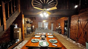 A dining area with a wooden table set for four, a stone fireplace, and a ceiling fan.
