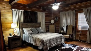 A wooden cabin bedroom with a bed, nightstand, lamp, chair, and a cowhide rug.