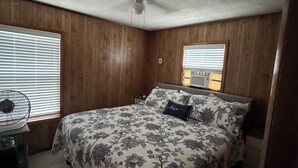 Une chambre à coucher avec un lit, un ventilateur de plafond et une fenêtre avec des stores.
