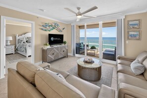 Sala de estar com sofá, mesa de centro, televisão e varanda com vista para o mar.