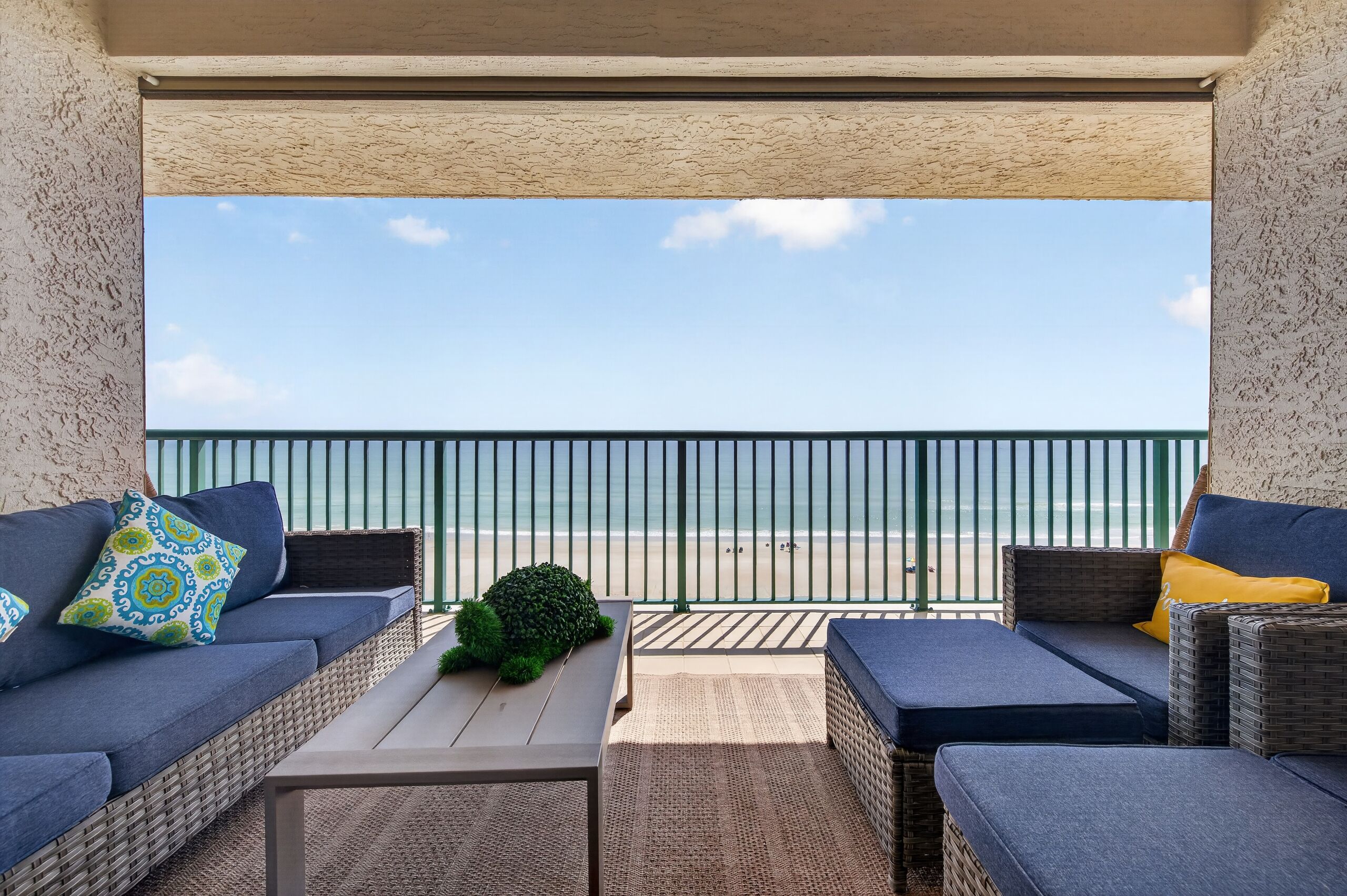 Un balcón con mobiliario de mimbre, una mesa y vistas a la playa.