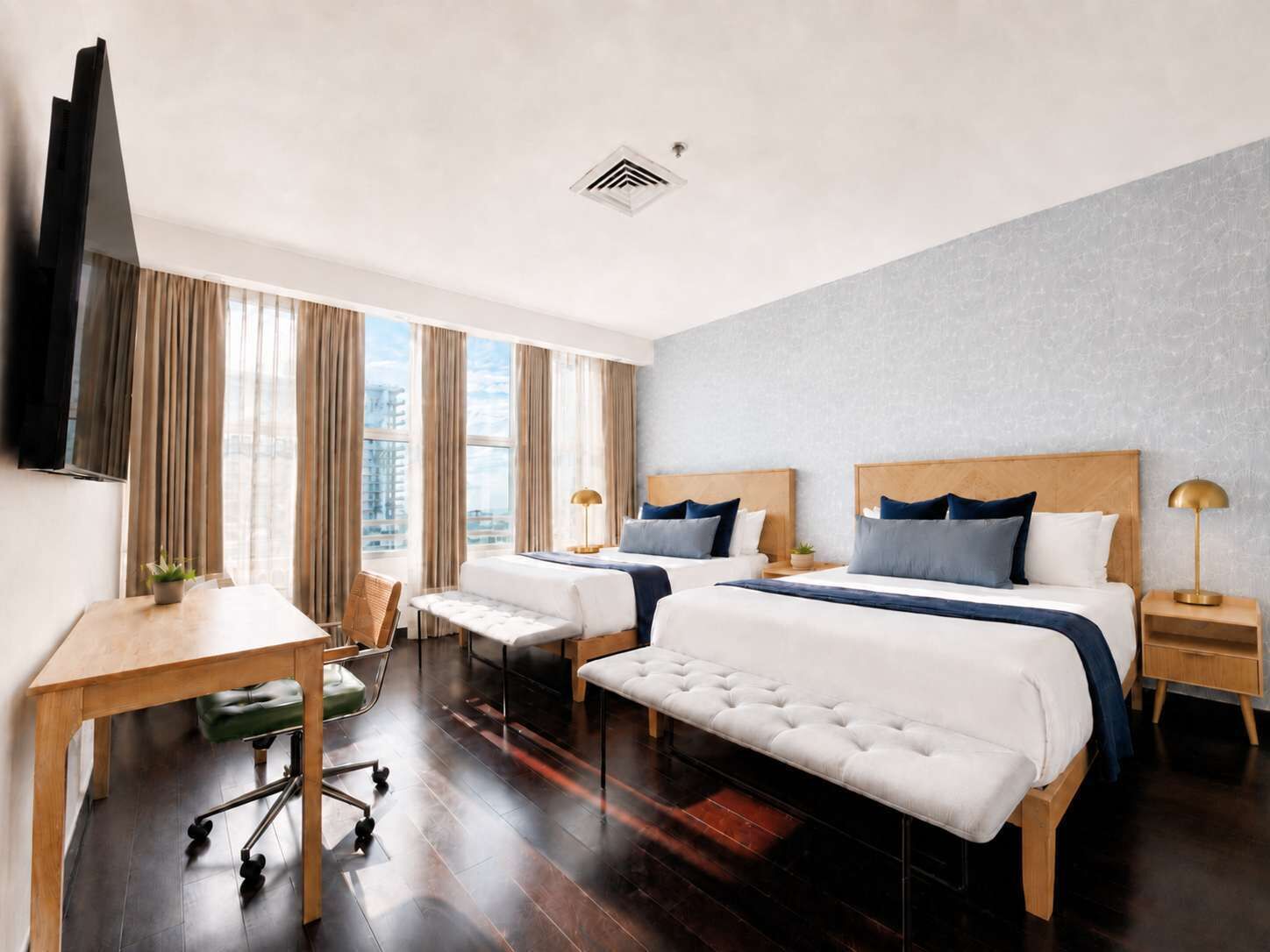 Habitación de hotel con dos camas, un escritorio, una silla, un televisor y una ventana con cortinas.