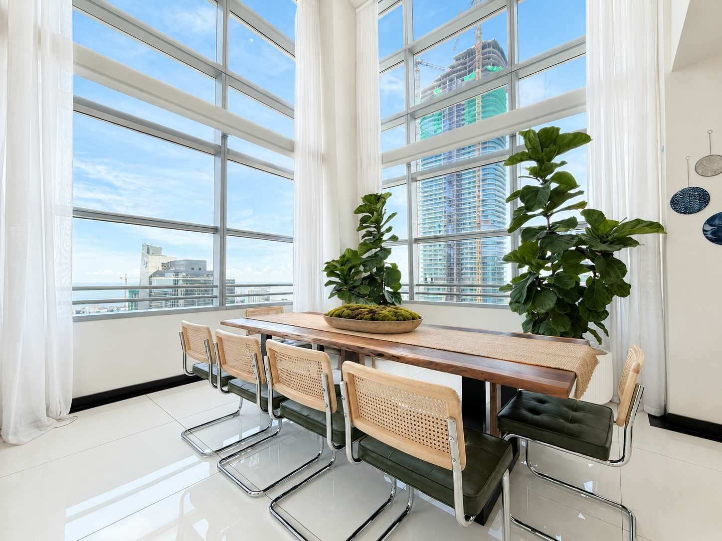 A modern dining area with a large window, a wooden table, and four chairs.