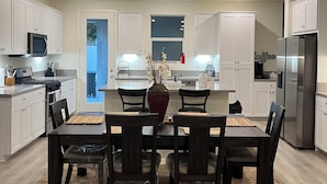 A modern kitchen with white cabinets, a dining table with chairs, and a refrigerator.
