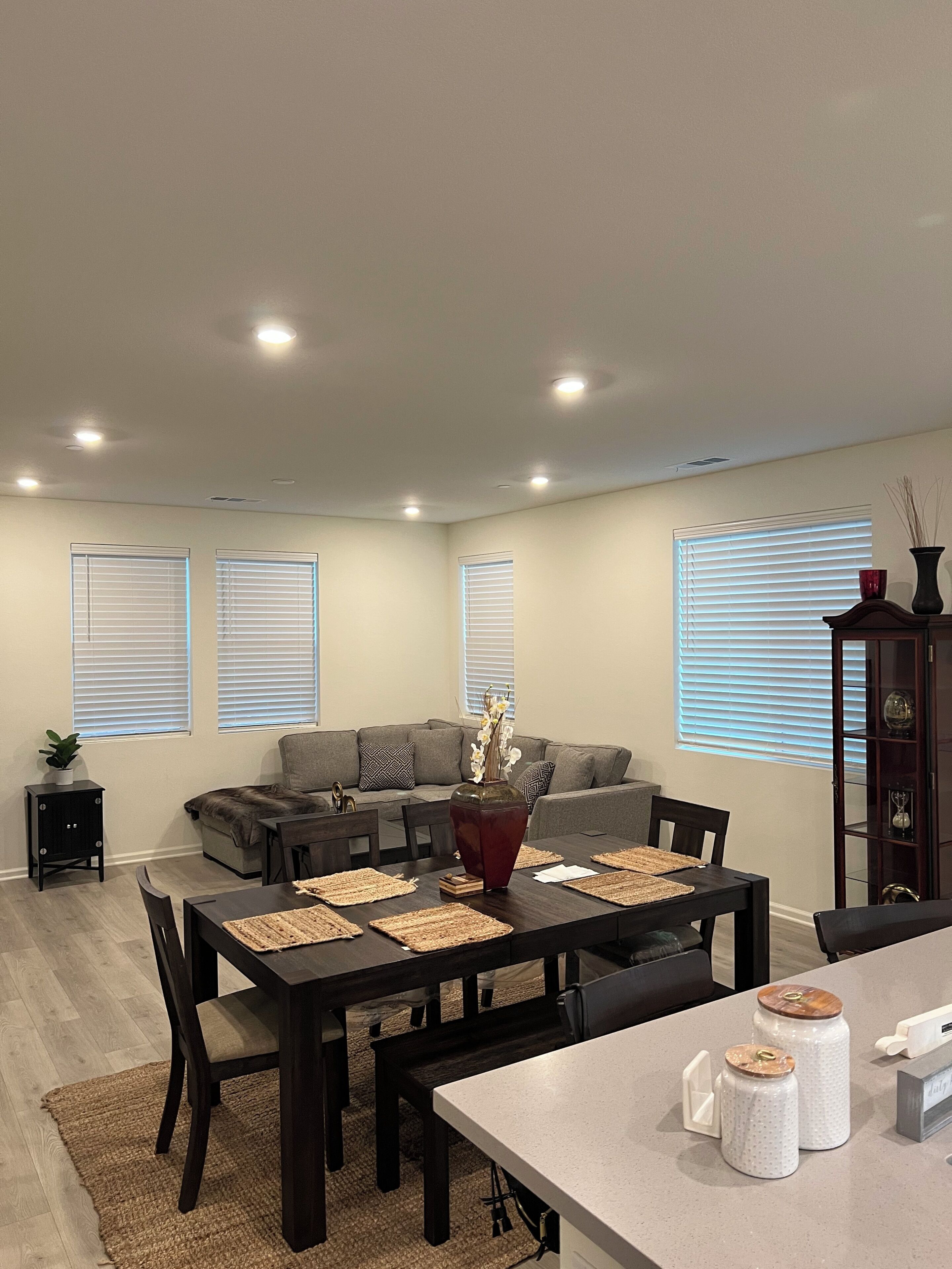 Una sala de estar moderna con una mesa de comedor de madera oscura, un sofá gris y un mueble con objetos decorativos.