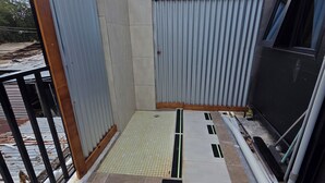Ein Balkon mit Metallgeländer, Fliesenboden und einer Wand aus Wellblech.