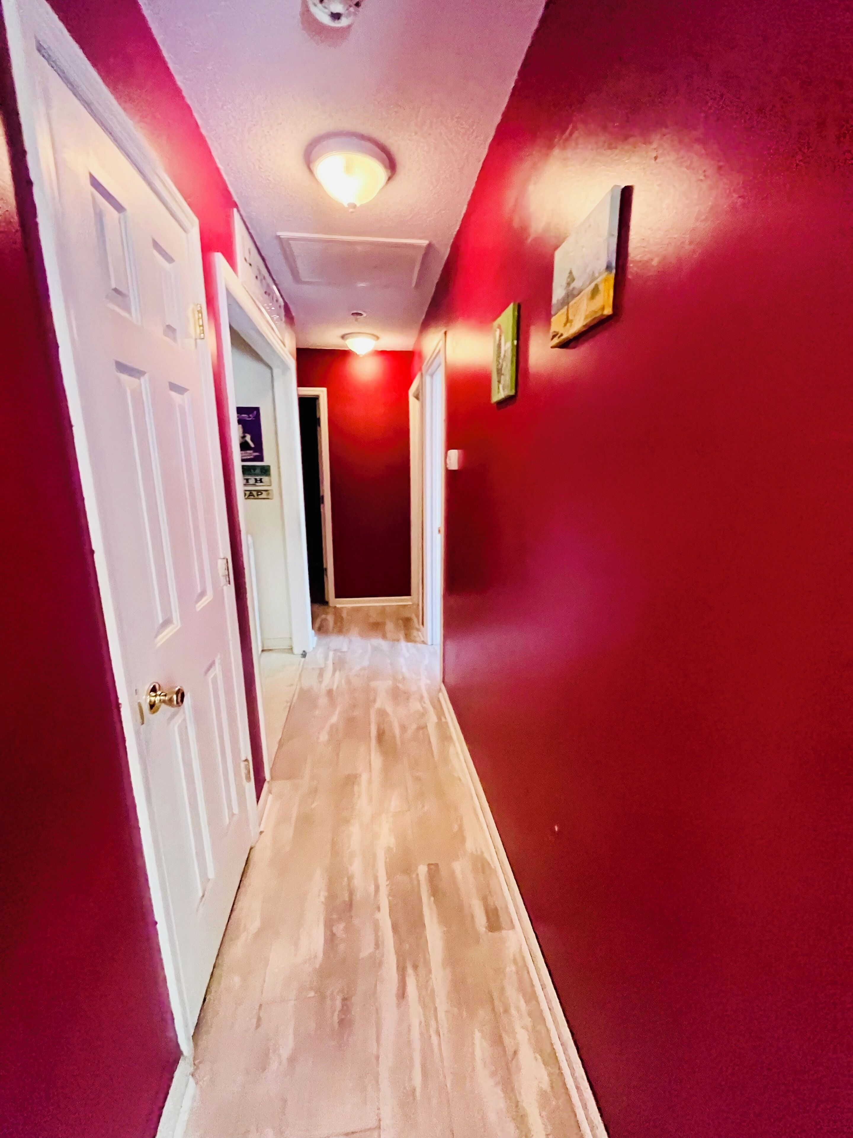 A hallway with red walls, white doors, and a wooden floor.