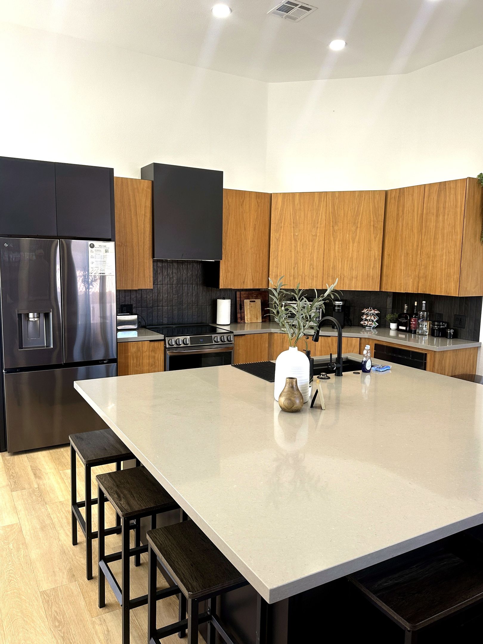 A modern kitchen with a large island, stainless steel appliances, wooden cabinets, and a flat-screen TV.