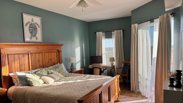 Een slaapkamer met een houten bed, een bureau, een stoel, een plafondventilator en een raam met gordijnen.