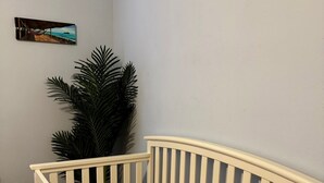 Een ledikant met een gestreept matras, een klein pluche speeltje en een potplant ernaast.