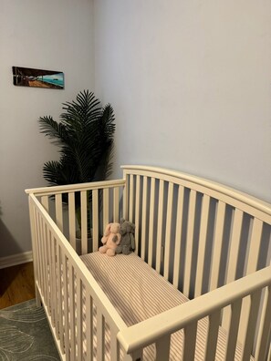 Ein Babybett mit gestreifter Matratze, einem kleinen Stofftier und einem Blumentopf daneben.