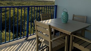 Een balkon met een tafel, stoelen, een lantaarn en uitzicht op groen en een heldere lucht.