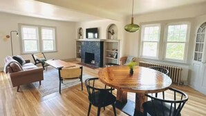 Un salon spacieux doté d’une cheminée, de parquet et d’une table à manger ronde.
