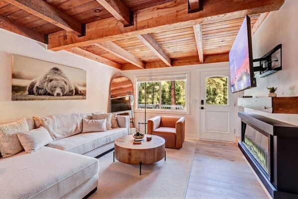 A modern living room with a sofa, armchair, and coffee table. There is a fireplace and a television mounted on the wall.