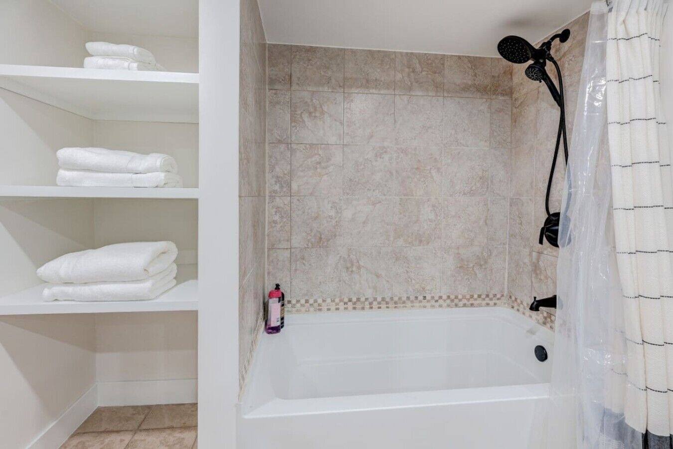 Une salle de bain avec une baignoire, des étagères avec des serviettes pliées, une pomme de douche et un rideau de douche.