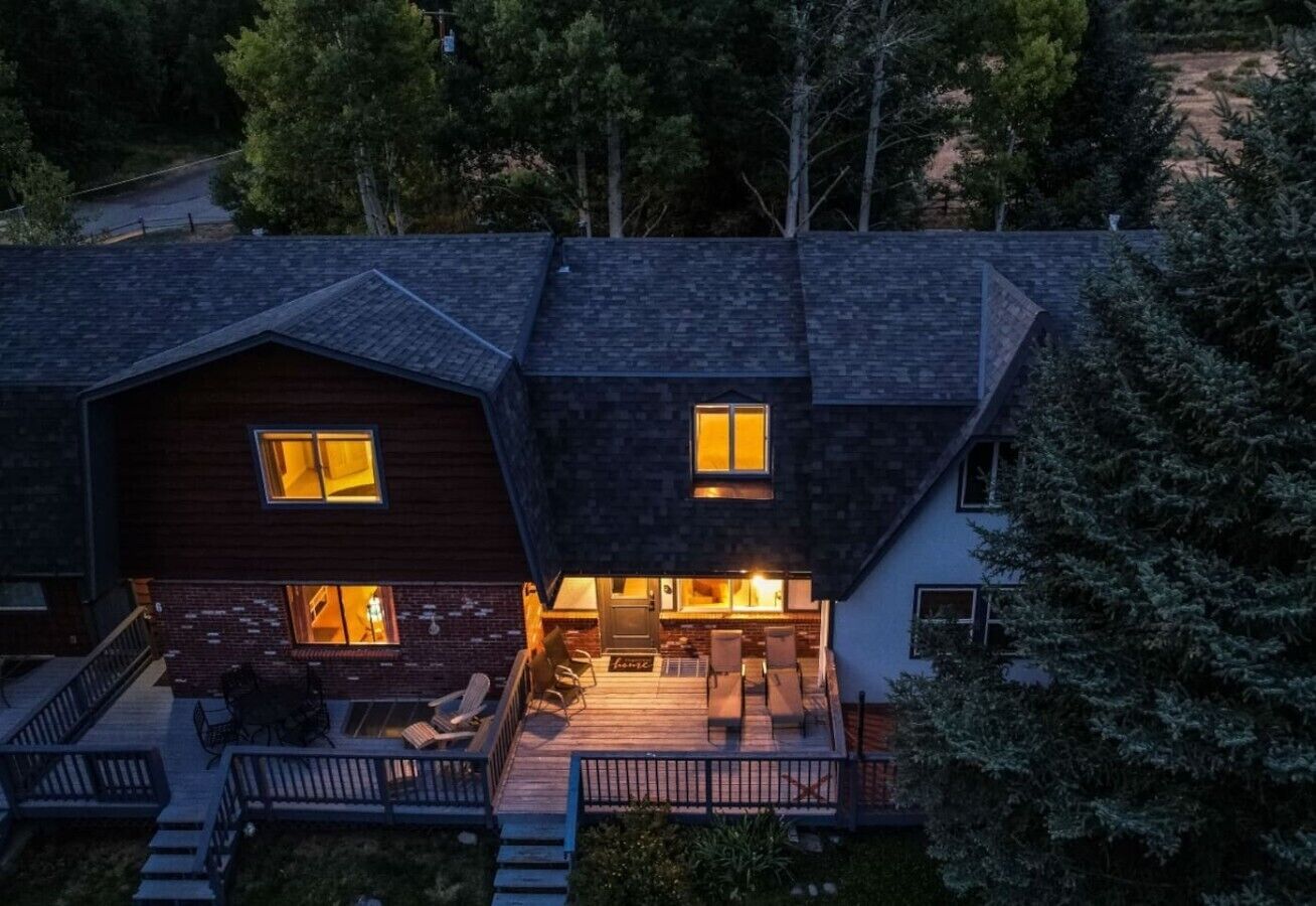 A two-story house with a covered patio area, a fireplace, and a deck with outdoor seating.