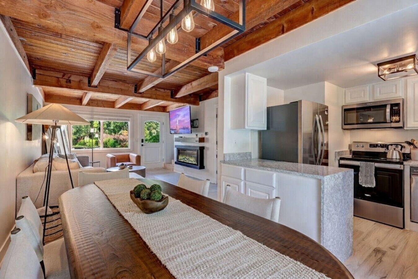 A modern kitchen with a central island, white cabinetry, stainless steel appliances, and a wooden ceiling.