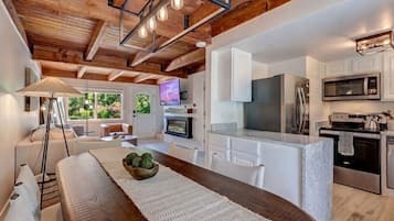 A modern kitchen with a central island, white cabinetry, stainless steel appliances, and a wooden ceiling.
