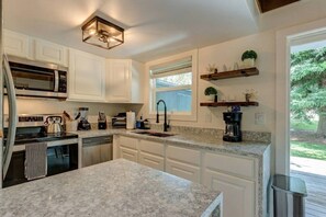 Una cocina con gabinetes blancos, encimera de granito, microondas integrado, estufa y cafetera.