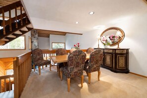 A dining area with a wooden table and patterned chairs, a wooden staircase, and a cabinet with a mirror. - Beaver Creek Escape | Hot Tub, Shuttle, Sleeps 10 (Beaver Creek)